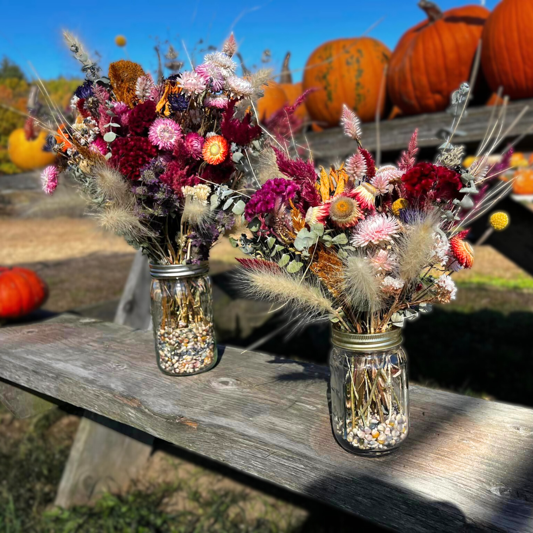 Multicolor dried floral arrangements in mason jars with colored ornamental corn filler.