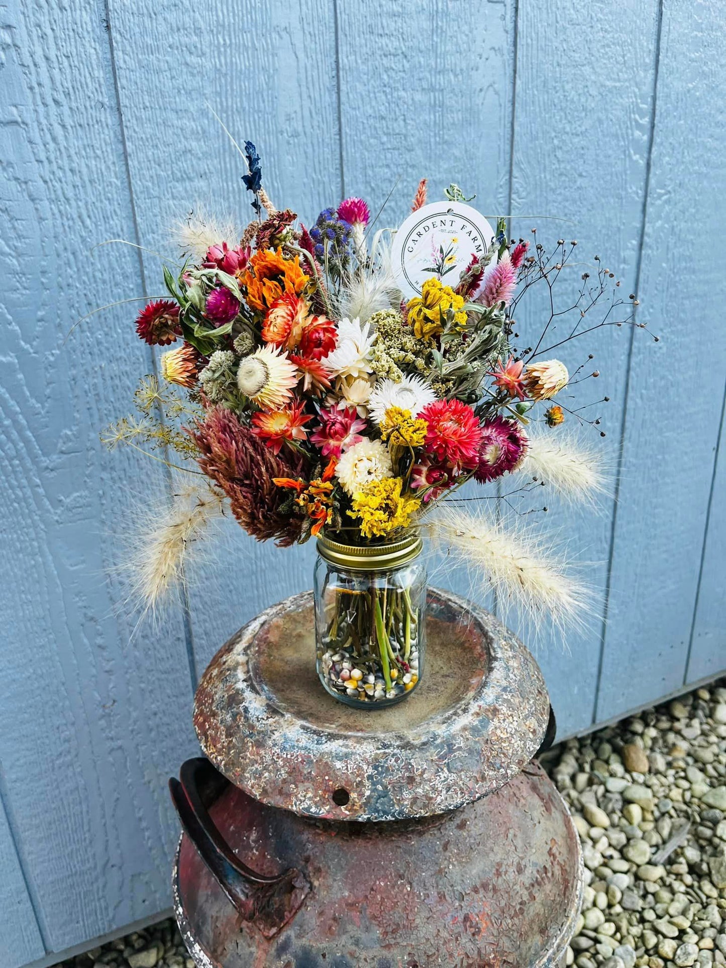 A large arrangement of dried flowers in a mason jar with ornamental corn fill.