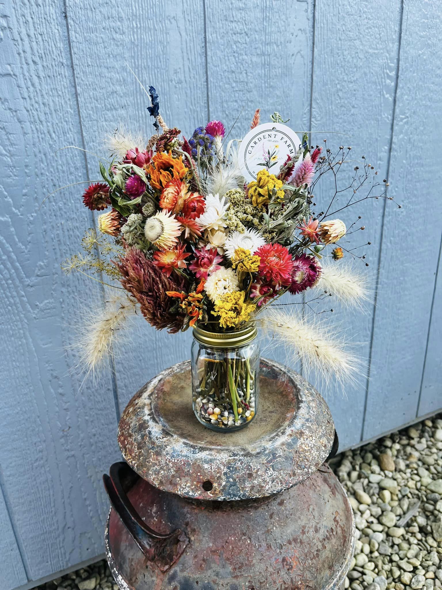 A large arrangement of dried flowers in a mason jar with ornamental corn fill.