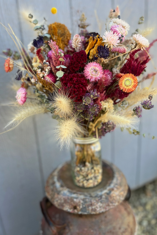 A large arrangement of dried flowers in marroon, cream, and salmon colors in a mason jar on a pedestal.