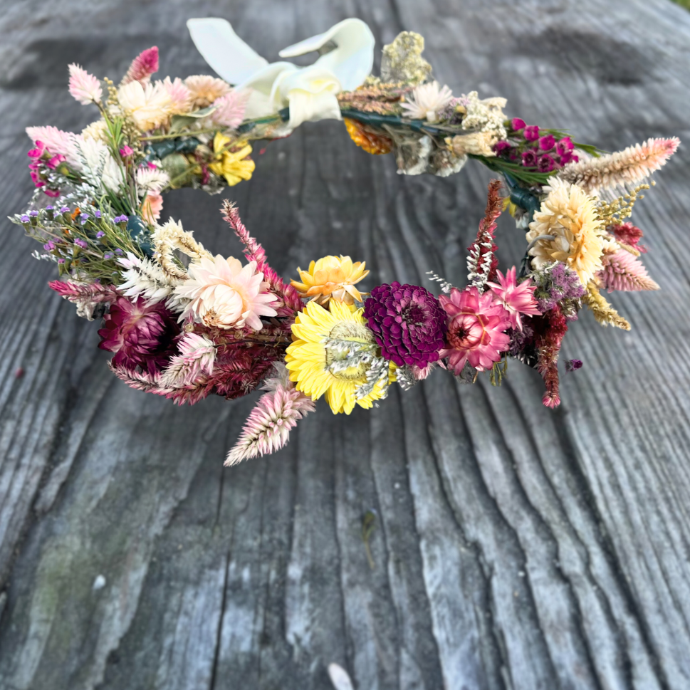 Closeup image of a handmade flower crown in pinks, maroons, and yellows sitting on a rustic picnic table.