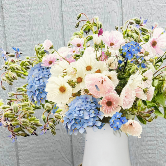 Wildflower arrangement in soft blue and white tones in a white vase.